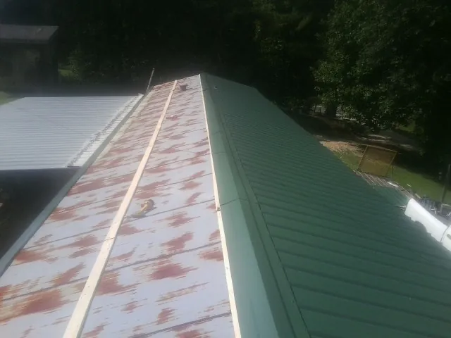 Old rusted panels beside newly installed green metal roofing — Wind Damage Roof Repair by Roofing Brothers in Winnemucca