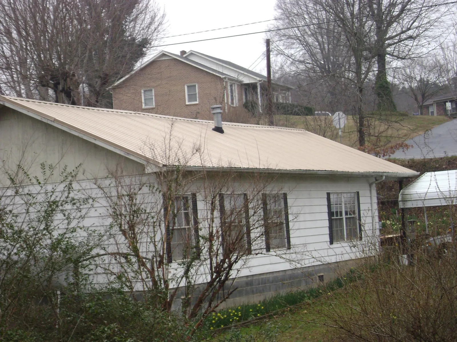 Tan metal roof on a white sided house set into a hillside — Commercial Roofing by Roofing Brothers in Winnemucca